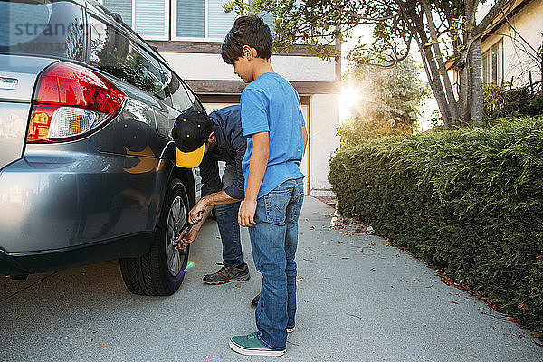 Sohn sieht Vater  der den Reifen mit einem Schraubenschlüssel in der Einfahrt spannt