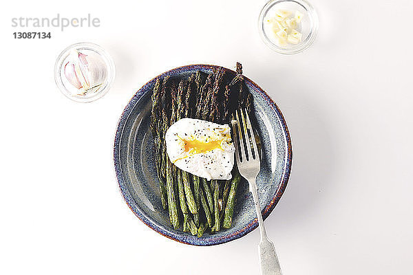 Draufsicht auf Ei mit Spargel  serviert in Tellern mit Knoblauch und Zwiebeln auf weißem Hintergrund