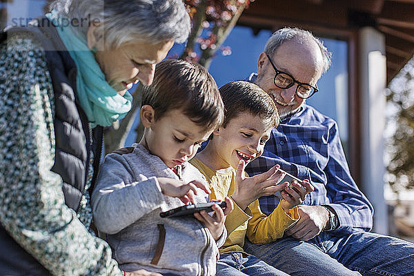 Glückliche Großeltern und Enkel benutzen Smartphones im Park
