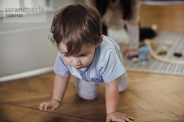Süßer kleiner Junge krabbelt auf dem Harwood-Fußboden mit der Mutter im Hintergrund
