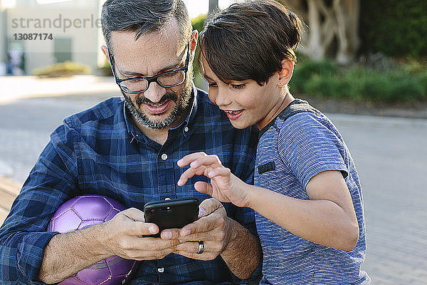 Vater mit Sohn benutzt Mobiltelefon im Park