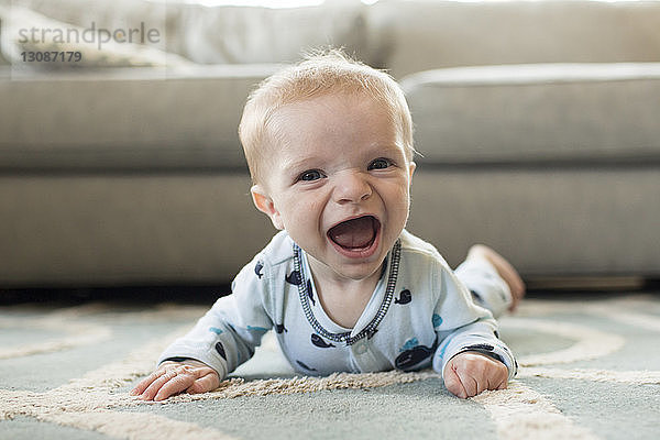 Porträt eines fröhlichen kleinen Jungen  der zu Hause auf einem Teppich liegt