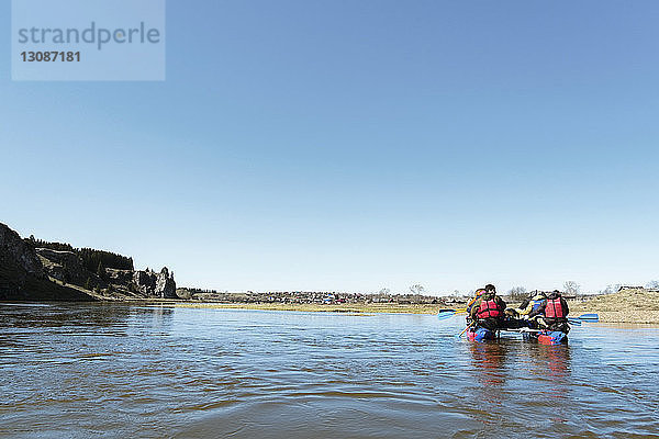 Rückansicht eines befreundeten Ruderbootes auf einem Fluss vor klarem blauen Himmel