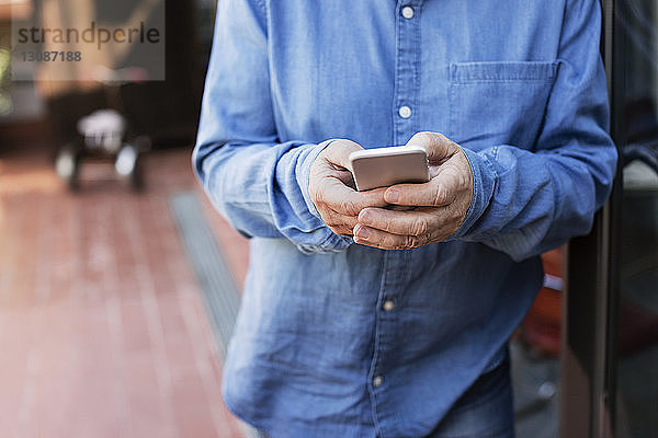 Mittelsektion eines älteren Mannes mit Smartphone auf der Veranda