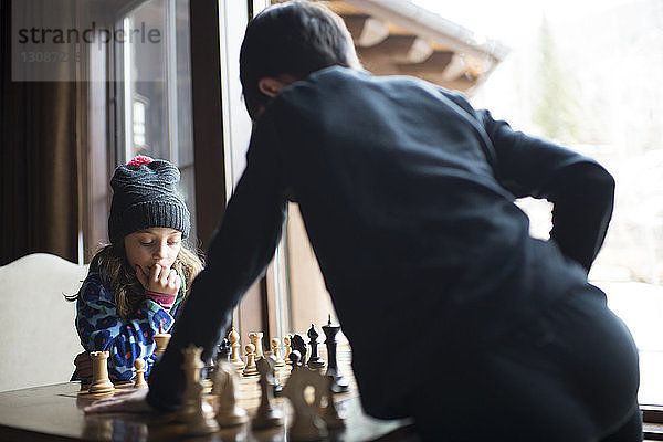 Geschwister spielen Schach  während sie zu Hause am Fenster stehen