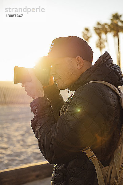 Mann fotografiert  während er bei Sonnenuntergang am Strand vor klarem Himmel steht