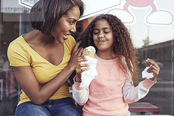 Mutter sieht ein Mädchen an  das Eiscreme genießt  während es auf dem Bürgersteig sitzt