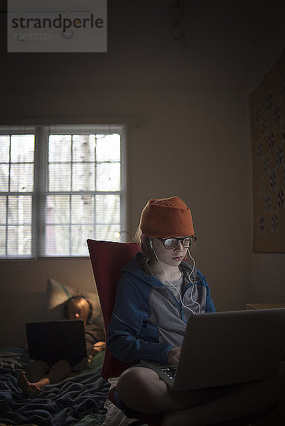 Junge benutzt Laptop-Computer  während er zu Hause auf einem Stuhl sitzt