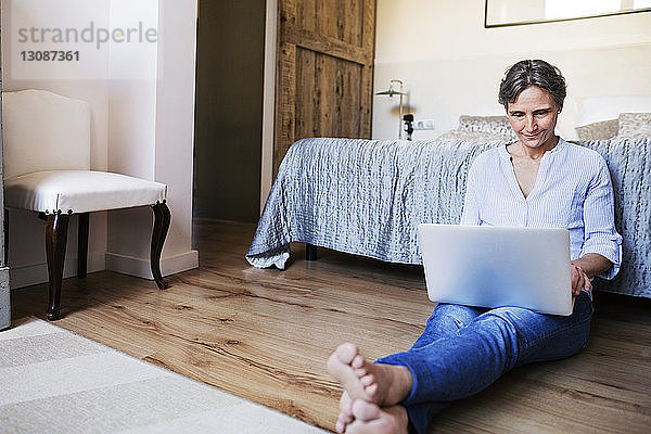 Reife Frau benutzt Laptop  während sie im Schlafzimmer auf dem Boden sitzt
