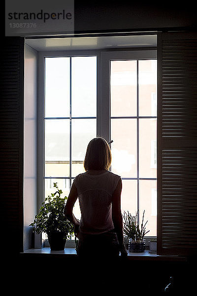 Rückansicht der am Fenster stehenden Frau