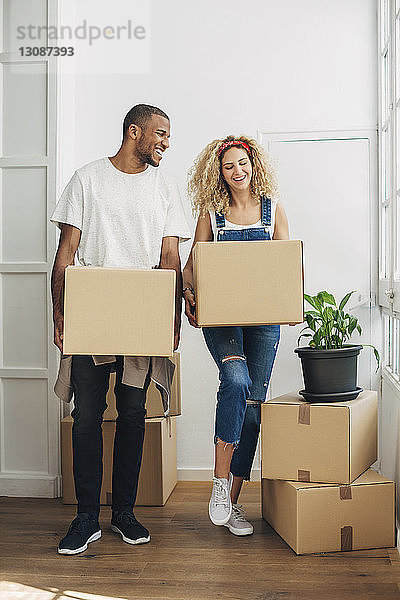 Glückliches Paar trägt Kartons  während es im neuen Haus auf dem Boden steht