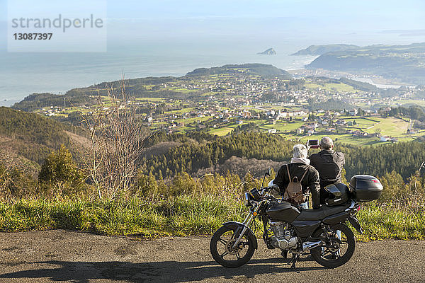 Älteres Ehepaar fotografiert Berge  während es mit dem Motorrad auf der Straße steht