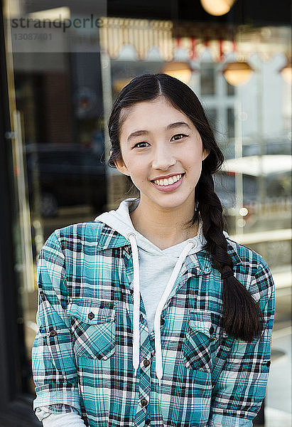 Porträt eines lächelnden  selbstbewussten Teenager-Mädchens mit geflochtenem Haar  das ein kariertes Hemd auf dem Markt trägt