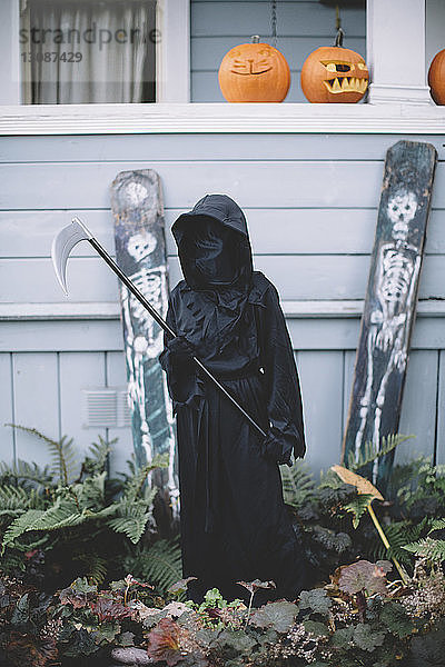 Junge in Halloween-Kostüm hält Waffe  während er im Hof beim Haus steht