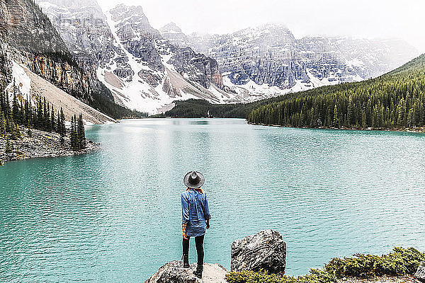 Rückansicht einer Frau mit Hut  die auf einem Felsen am Moraine Lake im Banff National Park steht