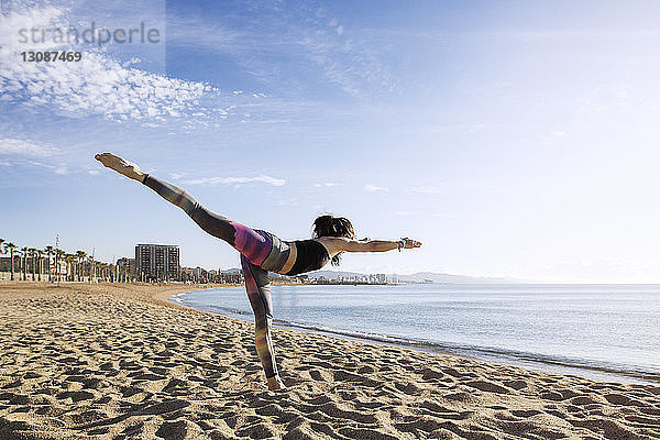 Entschlossene Frau  die am Strand Yoga in der Warrior 3-Pose macht