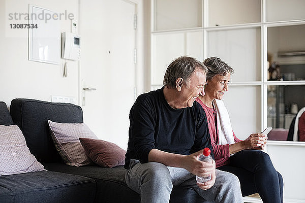 Glückliches sportliches Seniorenpaar benutzt Smartphone  während es zu Hause auf dem Sofa sitzt