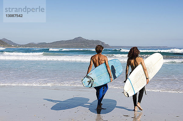 Rückansicht von Freunden  die an sonnigen Tagen Surfbretter am Strand tragen