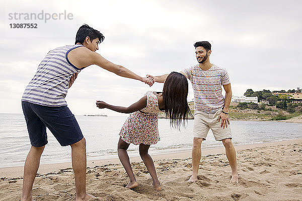 Frau geht beim Spielen am Strand unter den Armen der Männer vorbei