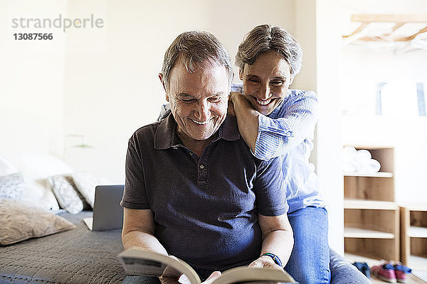 Fröhliches älteres Ehepaar liest Buch im Schlafzimmer