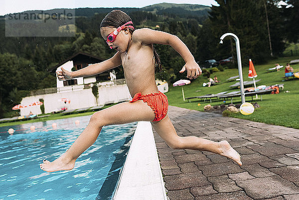Seitenansicht eines Mädchens ohne Hemd  das gegen den Berg in den Swimmingpool springt