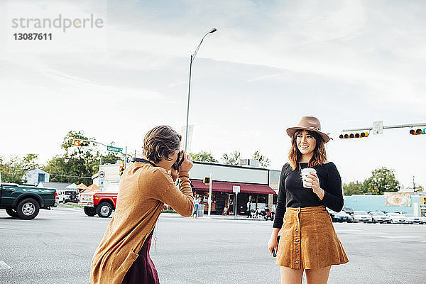 Frau fotografiert Freundin  während sie auf der Straße in der Stadt gegen den Himmel steht