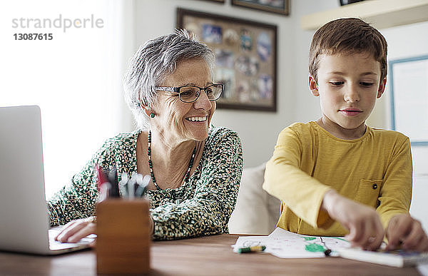 Glückliche ältere Frau schaut auf ihren Enkel  der zu Hause Buntstifte auswählt