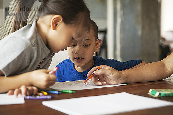 Kinder sehen Mutter beim Zeichnen auf Papier an  während sie im Wohnzimmer sitzen