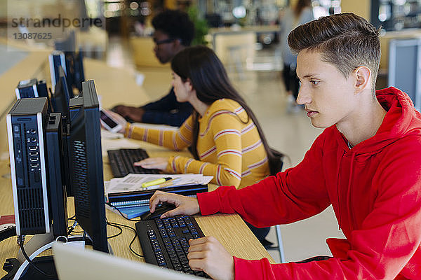 Freunde nutzen Desktop-Computer  während sie in der Bibliothek am Tisch sitzen
