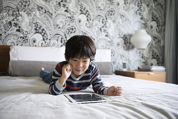 Glücklicher Junge benutzt digitales Tablett im Bett