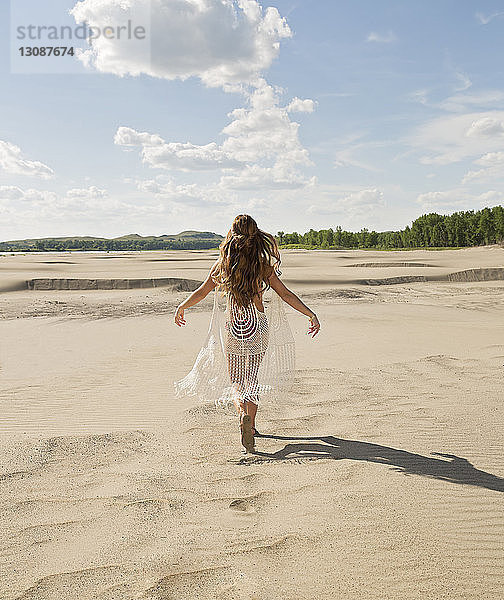 Rückansicht einer jungen Frau im Bikini  die auf Sand am Strand gegen den Himmel läuft