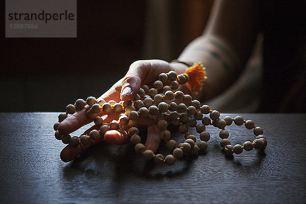 Beschnittenes Bild einer Frau  die zu Hause in der Dunkelkammer Gebetsperlen hält