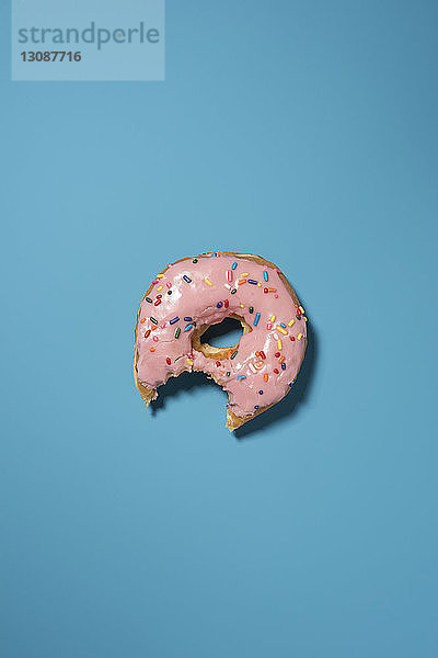 Draufsicht auf den Biss eines gegessenen Donuts auf blauem Hintergrund