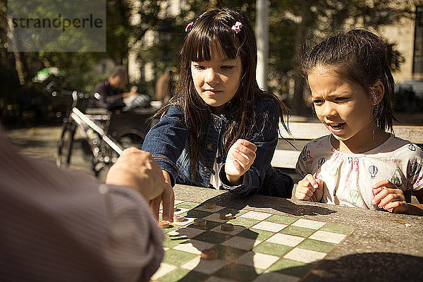 Schwestern spielen mit Großvater Dame  während sie im Park am Tisch sitzen