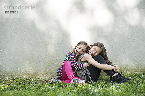 Seitenansicht eines Mädchens  das seine Schwester umarmt  während es im Hof an der Wand sitzt