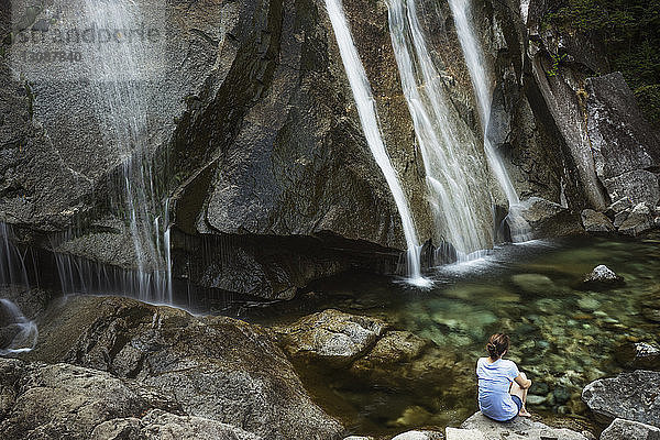 Rückansicht einer Frau  die auf einem Felsen vor Wasserfällen sitzt