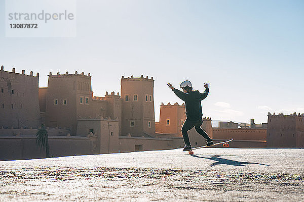 Mann fährt bei Sonnenschein in voller Länge Skateboard gegen die Burg