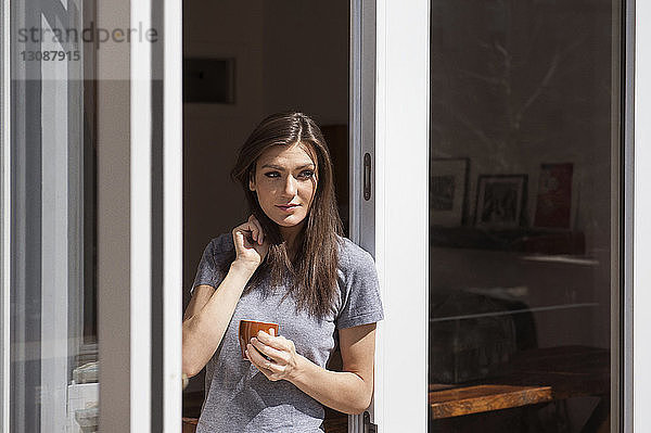 Schöne Frau hält Kaffeetasse und steht am Fenster