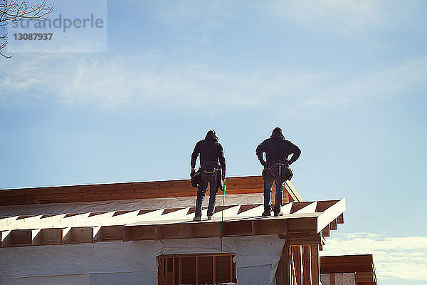 Niedrigwinkelansicht von Arbeitern  die auf einem Dachbalken gegen den Himmel stehen