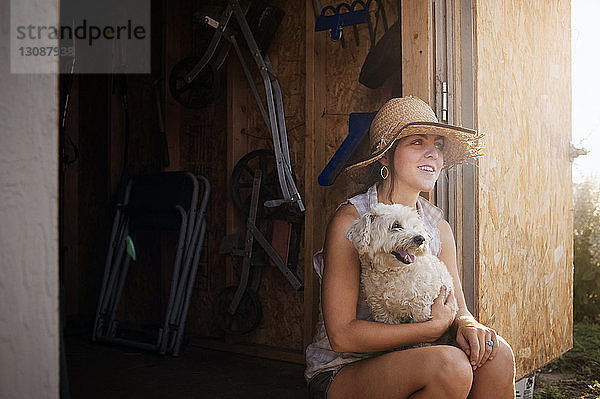 Nachdenkliche Bäuerin sitzt mit Hund in Hütte auf dem Feld