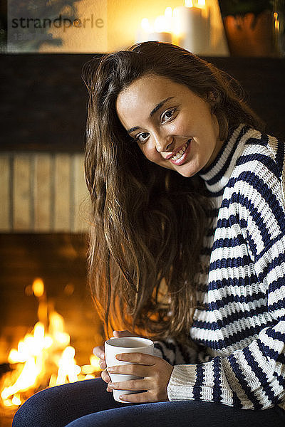 Porträt einer lächelnden Frau  die zu Hause sitzt und eine Kaffeetasse hält