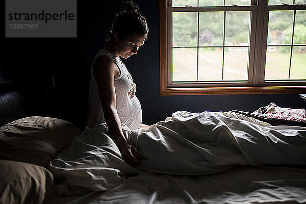 Seitenansicht einer schwangeren Frau  die zu Hause den Bauch am Bett berührt