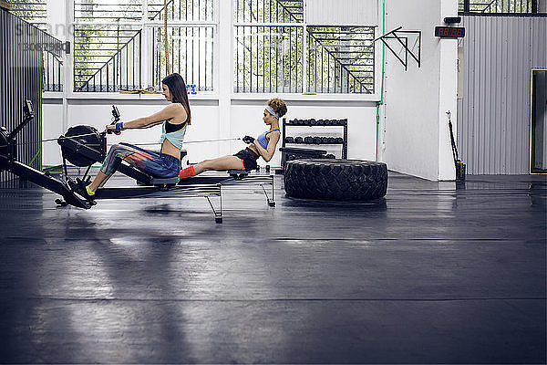 Seitenansicht von Sportlerinnen  die im Fitnessstudio auf einem Rudergerät trainieren