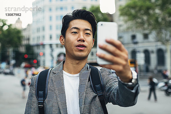 Geschäftsmann mit Rucksack  der sich im Stehen auf einem Fußweg durch ein Smartphone trägt