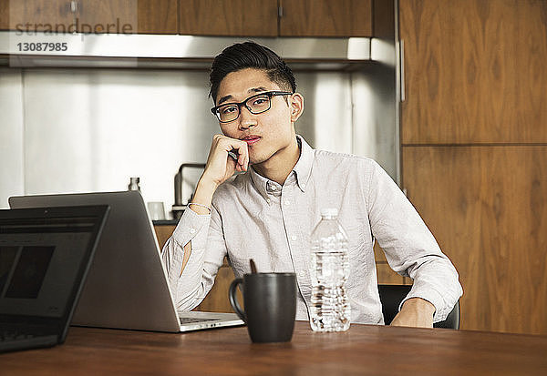 Selbstbewusster Geschäftsmann mit Laptop-Computer am Tisch im Kreativbüro