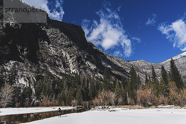 Wanderer  der im Yosemite-Nationalpark im Winter am Fluss auf Schnee gegen die Berge steht