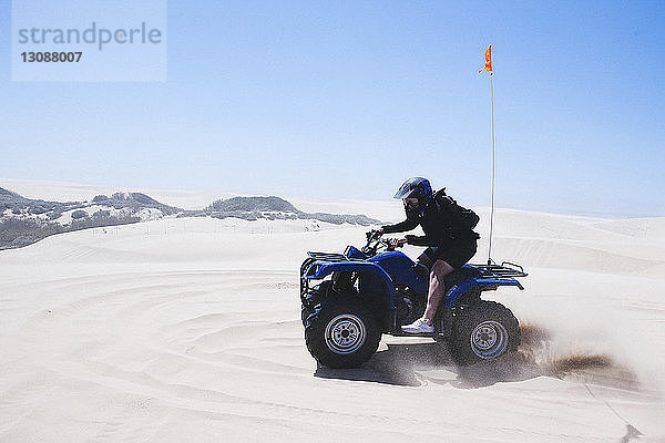 Ein junger Mann fährt in voller Länge Quad am Strand von Pismo Beach vor klarem Himmel bei strahlendem Sonnenschein