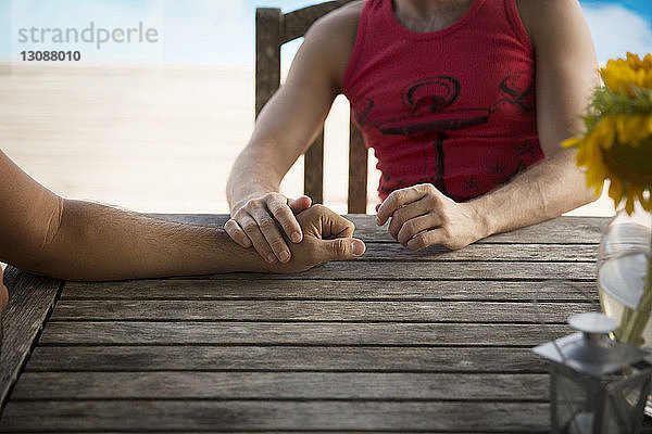 Ausgeschnittenes Bild eines homosexuellen Paares  das sich an einem Holztisch im Resort ausruht
