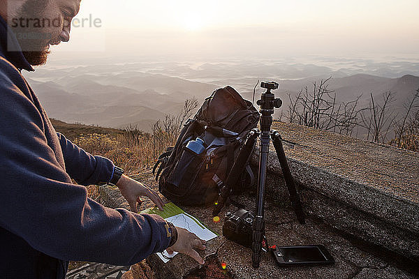 Mann liest auf der Karte  während er bei Sonnenuntergang auf einem Berg steht