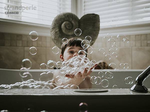 Junge spielt mit Seifenblasen beim Baden in der Badewanne